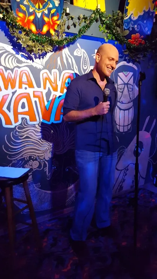 Eitan on stage with a microphone at a kava bar